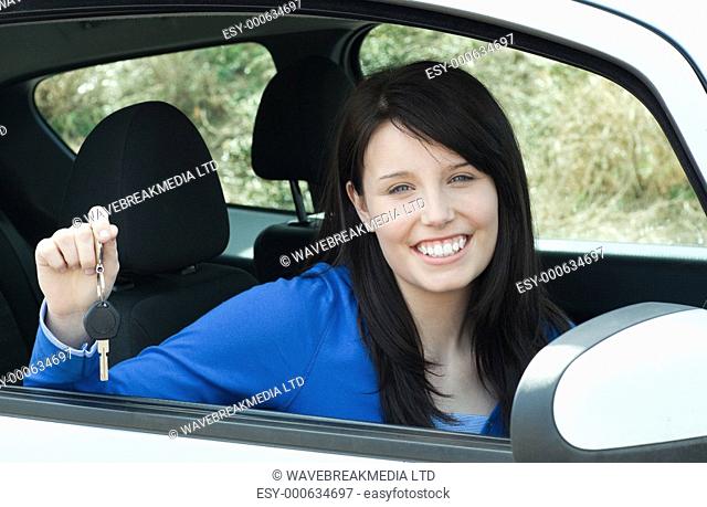 Jolly teen girl sitting in her car holding keys after bying a new car