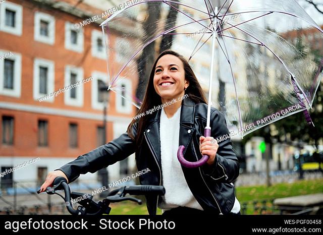 Woman holding umbrella while riding bicycle at street in city