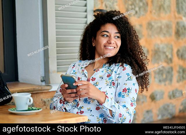 Thoughtful smiling young woman sitting with mobile phone at cafe