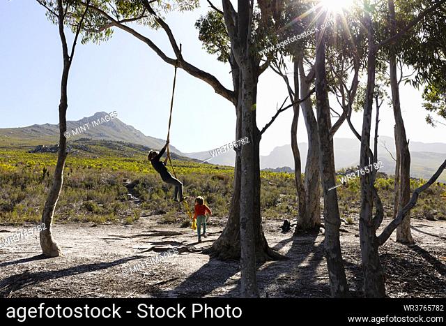 Teenage girl and younger brother using rope swing on a hiking trail