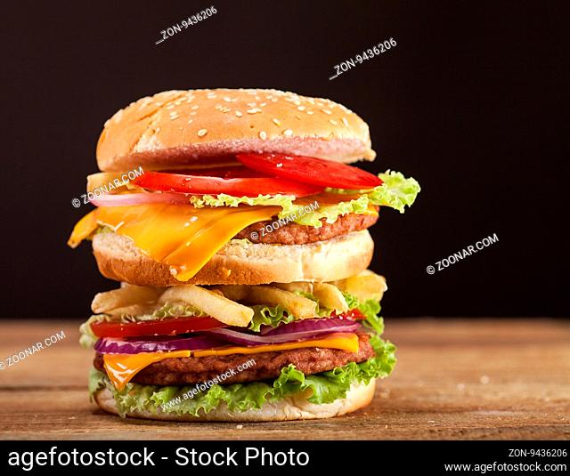 Fresh delicious burger with cheese, tomato, onion and lettuce on wooden table and brown background
