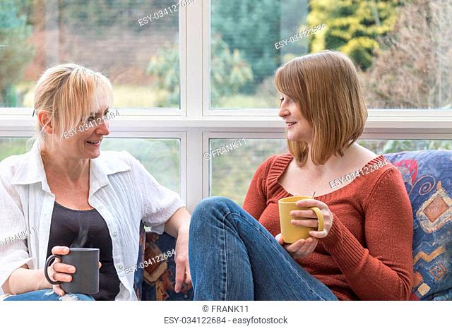 Middle aged woman and a young woman are chatting together sitting on the sofa in the conservatory