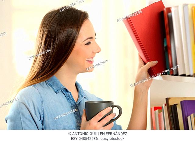 Happy woman choosing a book from a shelving at home