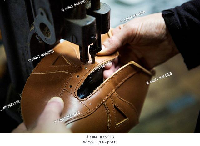 Close up of worker in a shoemaker's workshop, using a machine to punch holes into a leather shoe