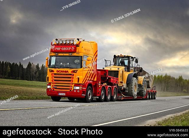 Customised Scania G580 truck of PHP Group in front of gooseneck trailer transports Cat wheel loader on Highway 10. Tammela, Finland. May 14, 2021
