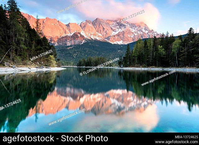 The morning view over the Eibsee with the Zugspitze, which is reflected in the water. The Sasseninsel is located in the lake