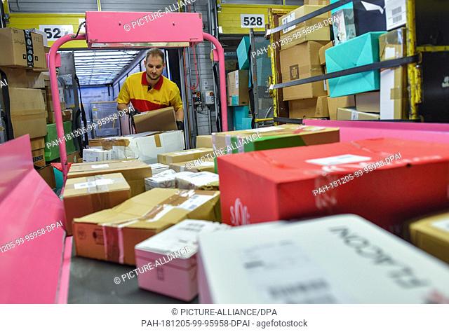 05 December 2018, Brandenburg, Rüdersdorf: Matthi Lippert, employee at the DHL-Paketzentrum, takes shipments from a conveyor belt