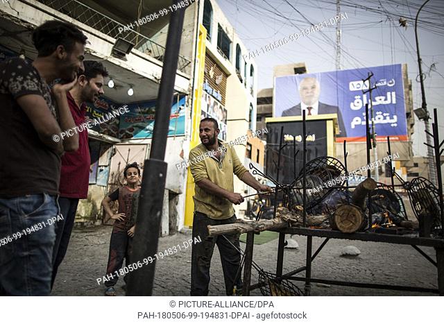 A picture made available on 07 May 2018 shows a man selling grilled fish backdropped by a campaign poster of Iraqi Prime Minister Haider al-Abadi in Baghdad