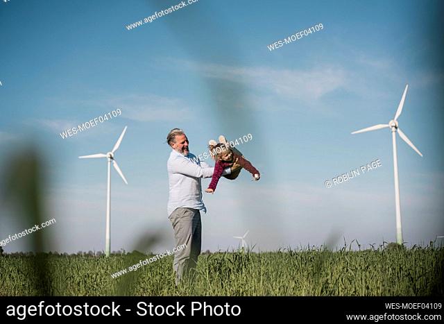Playful man carrying daughter enjoying in field on sunny day