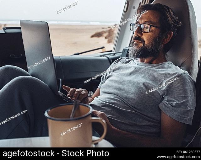 Concept of travel lifestyle modern people and smart working digital nomad job activity. Handsome man use laptop computer sitting and relaxing inside a camper...