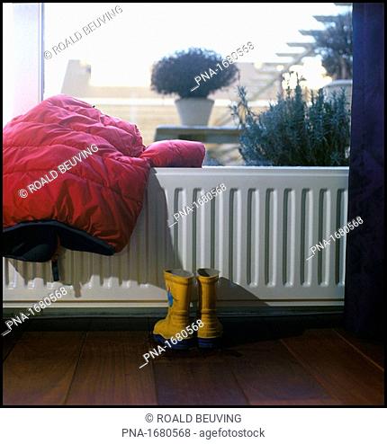 A childrens jacket and rain boots are drying near the central heating in the living room