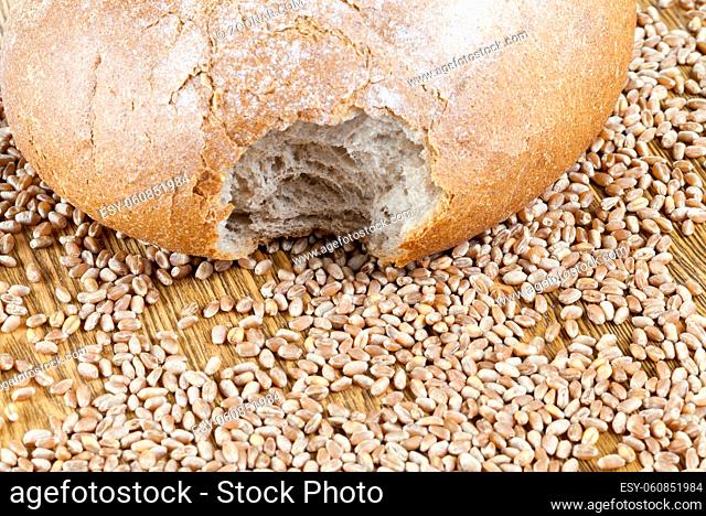 a bitten loaf of wheat bread lying on a wooden table along with whole grains. close-up photo