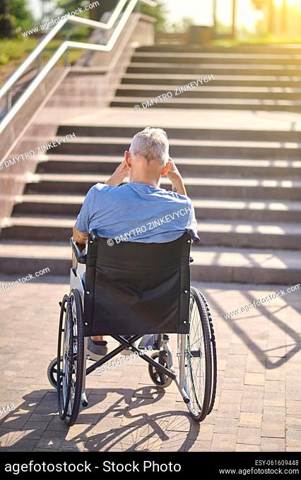 Disabled man. A man in a wheel chair sitting backside near the stairs outdoors
