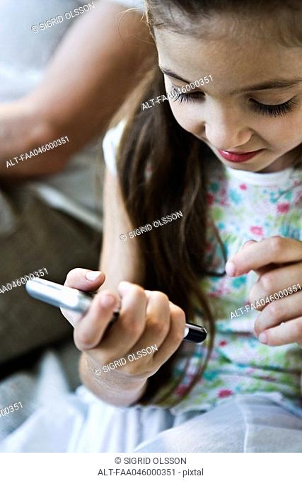 Little girl looking at cell phone, woman in background