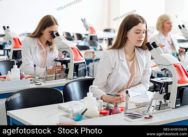 Researchers in white coats working with microscopes in lab