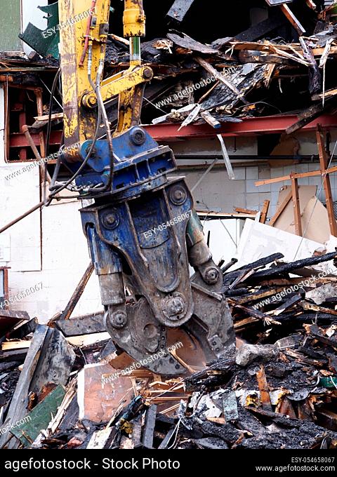 a demolition claw removing debris and rubble from a wrecked building damaged by fire