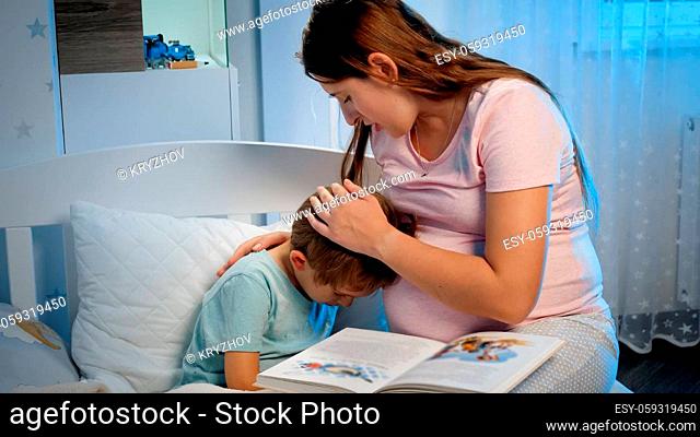 Young pregnant mother hugging and soothing her crying little boy lying in bed at night. Caring and loving parent hugging child