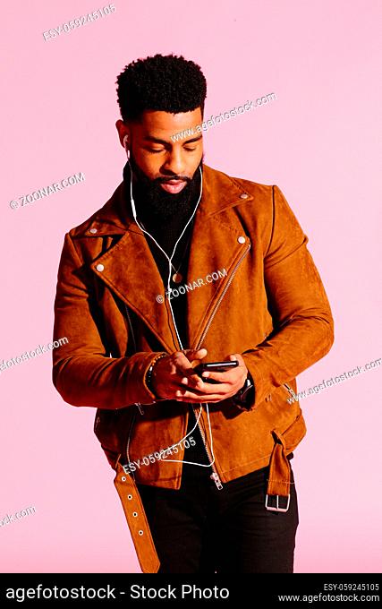 Stylish, handsome and cool African American man with beard, listening to music, isolated on pink studio background