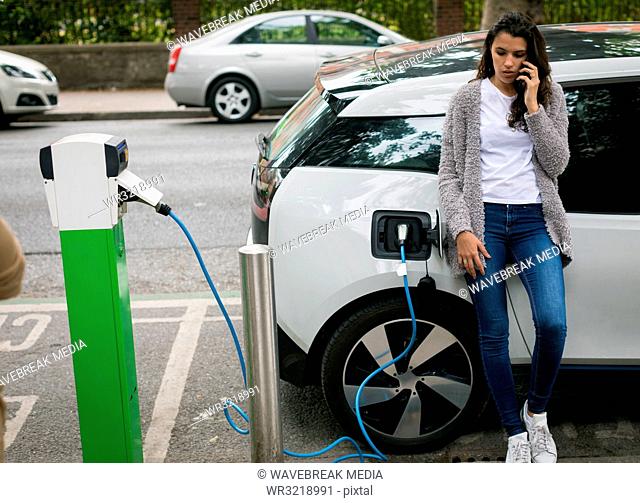 Woman talking on mobile phone while charging electric car