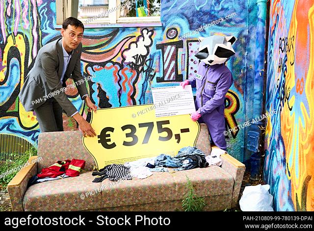 09 August 2021, Berlin: Neukölln's district mayor Martin Hikel (l, SPD), together with the district mascot, holds an oversized price tag over a couch that was...
