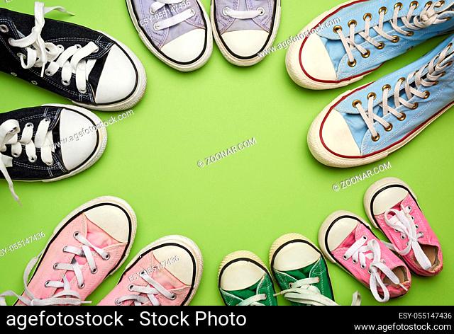 many multi-colored well-worn textile sneakers of different sizes on a green background, top view, concept, family and team, friendship, copy space