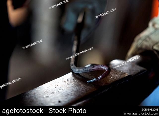 blacksmith bending hot iron on the anvil