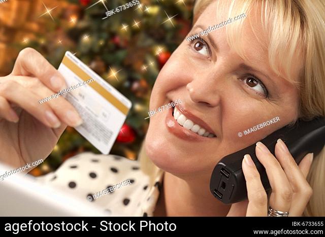 Beautiful woman on the phone holding her credit card in front of christmas tree and laptop computer