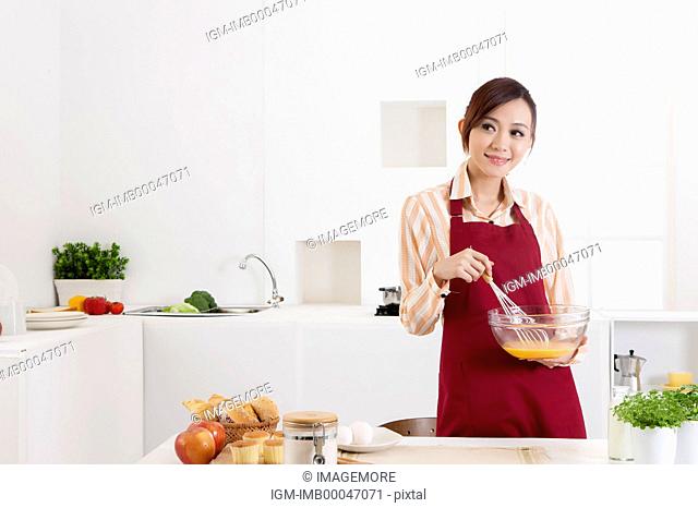 Young woman holding wire whisk for eggs and smiling at the camera