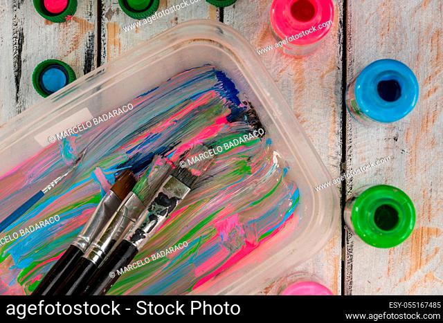 palette and acrylic colors next to small brushes on rustic table