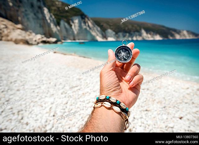 Hand holding a compass on the beach in background