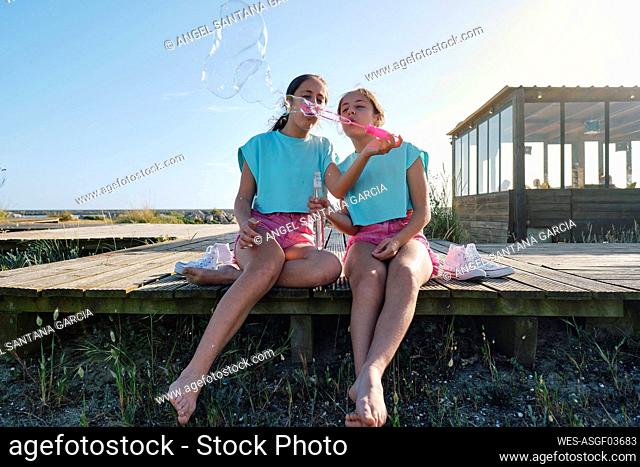 Twin sisters blowing bubbles on jetty at beach