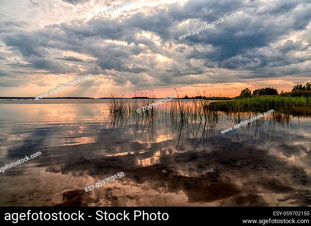 A colorful sunset and expressive sky reflections in a calm and peaceful lake with reeds in the foreground