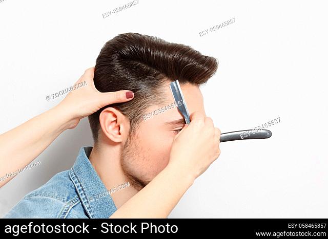 Hairdresser cutting black hair of handsome man with blade. Modern hairdressing technologies. Studio shot. White background