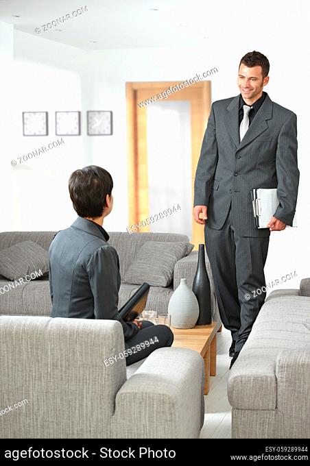 Business meeting at office lobby, young businessman arriving, smiling