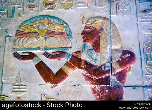 An ancient egyptian hieroglyphic painted carving showing the Pharoah Seti making an offering to the gods of a tray of food including fruit and poultry