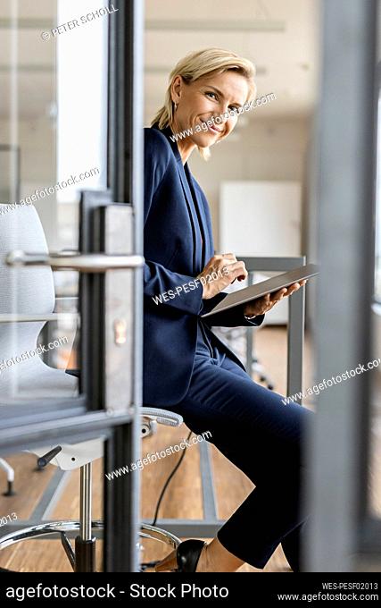 Portrait of smiling blond businesswoman using tablet in conference room