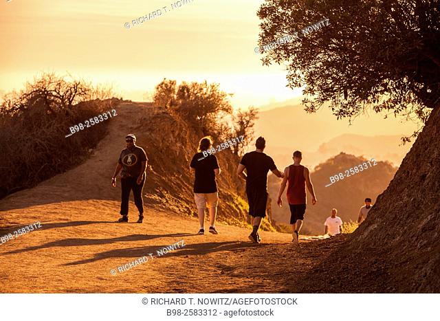 A small group of people walking on a hiking trail at sunset in the Hollywood Hills of Griffith Park, Los Angeles