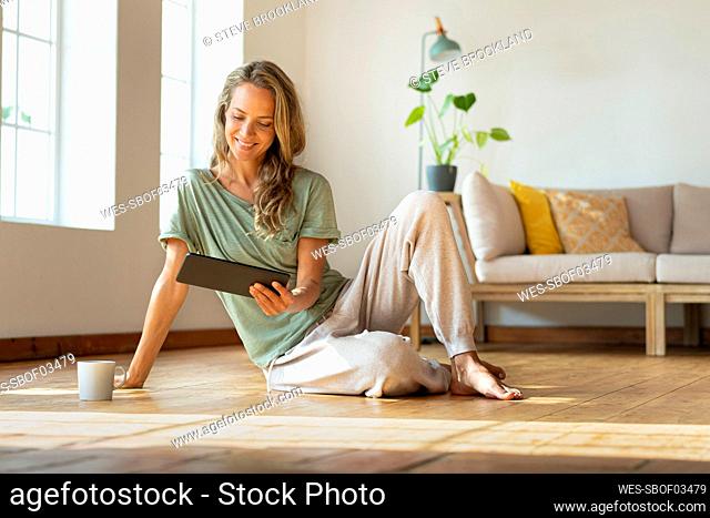 Smiling woman looking at digital tablet while sitting on floor