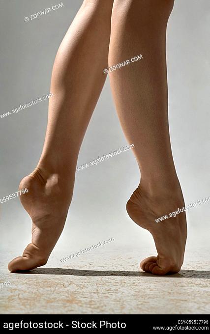 Closeup photo of barefoot legs of the ballerina in the studio on the gray background. She stands on the toes. Closeup. Vertical