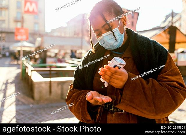 Italy, Woman in face mask using hand sanitizer on city street