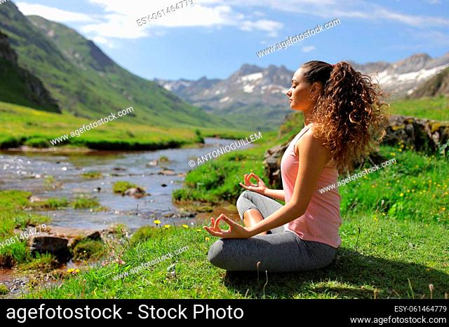 Side view full body portrait of a yogi doing yoga exercise in a riverside in a green mountain