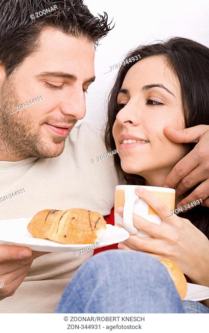 Junger Mann streichelt seiner Freundin beim Frühstück zart über ihre Wange Model l.: Kosta Lales - Model r.: Dimitra Vlahou