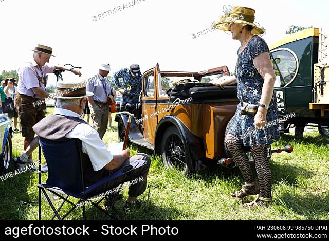 08 June 2023, Bavaria, Maxlrain: Participants in matching outfits stand with their vehicles at southern Bavaria's largest classic car meeting in front of the...