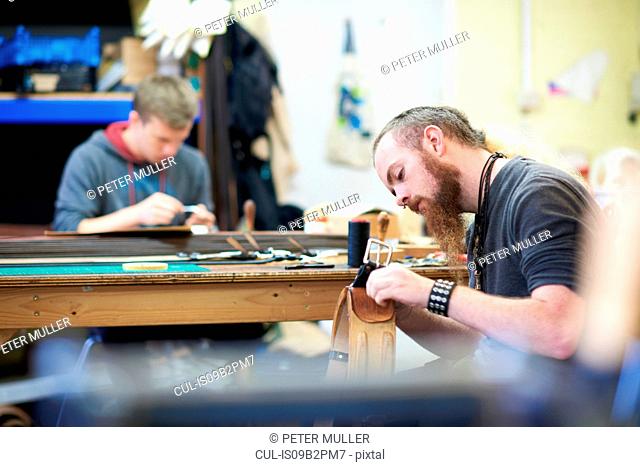 Male worker in leather workshop, sewing up seams around a belt buckle