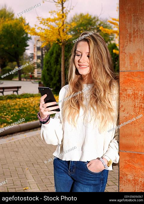 Young cheerful fitness woman on the street and consulting her mobile phone