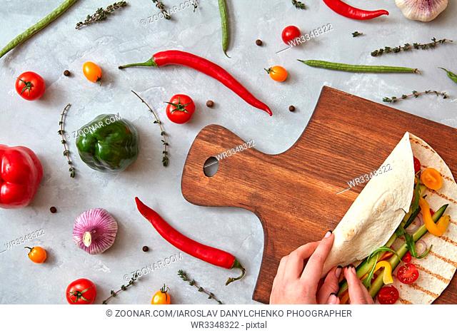 A woman makes a burrito with fresh vegetables on a wooden board. A step-by-step recipe for cooking. Top view, flat lay