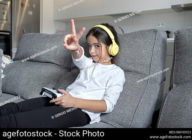 Little girl doing peace sign while playing video game in living room