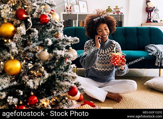 Happy woman with Christmas present talking on mobile phone in living room