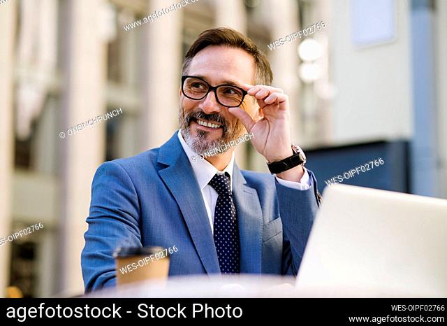 Smiling mature businessman adjusting eyeglasses sitting in cafe