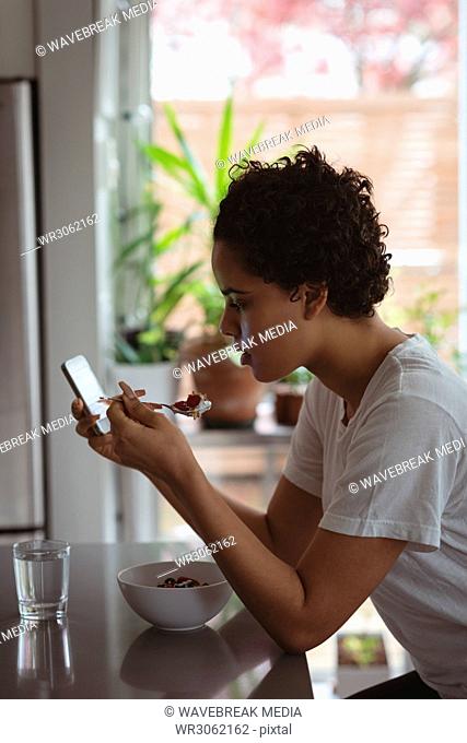 Woman having breakfast while using mobile phone
